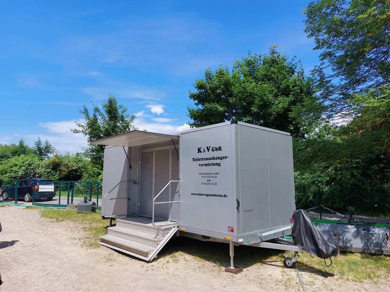Toilettenanhänger im sommerlichen Garten neben einer Hecke