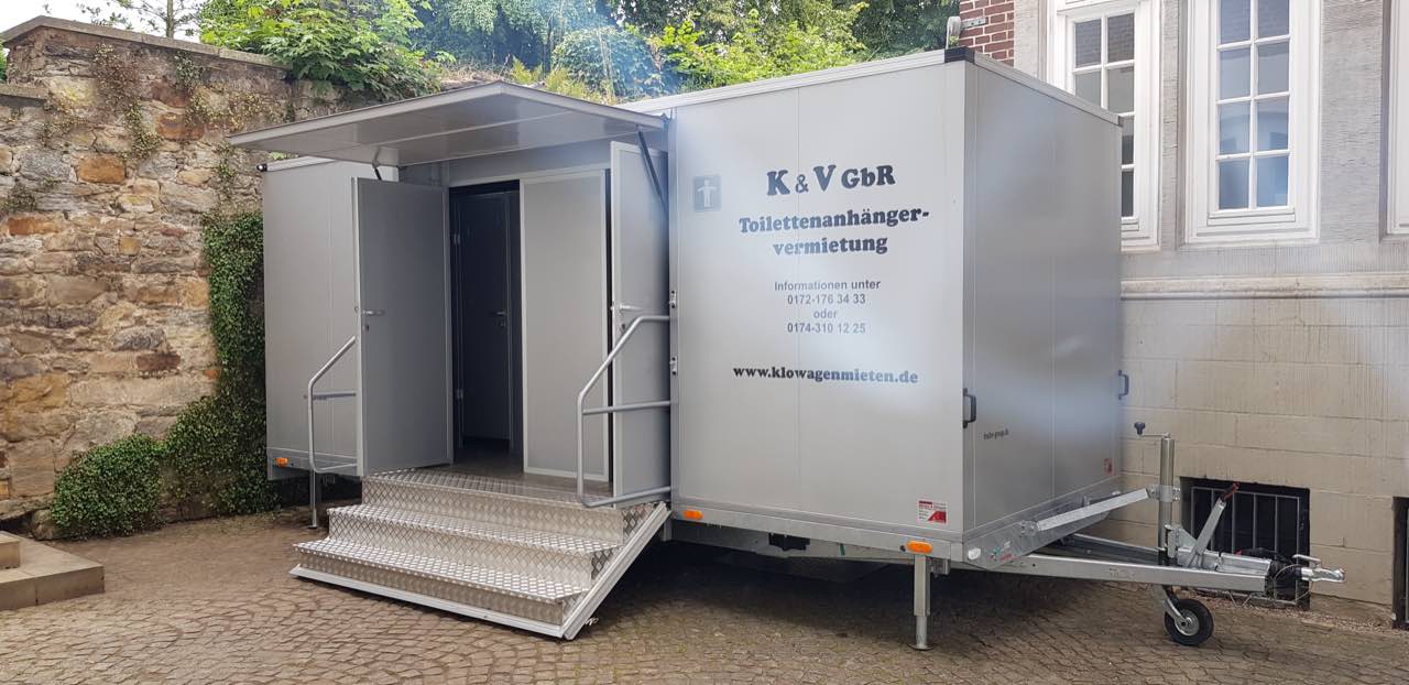 Toilettenanhänger in einem Innenhof mit Natursteinmauer