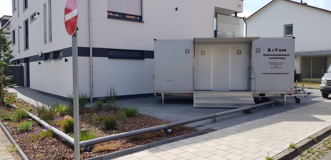 Toilettenanhänger vor einem Neubau in einem Wohngebiet