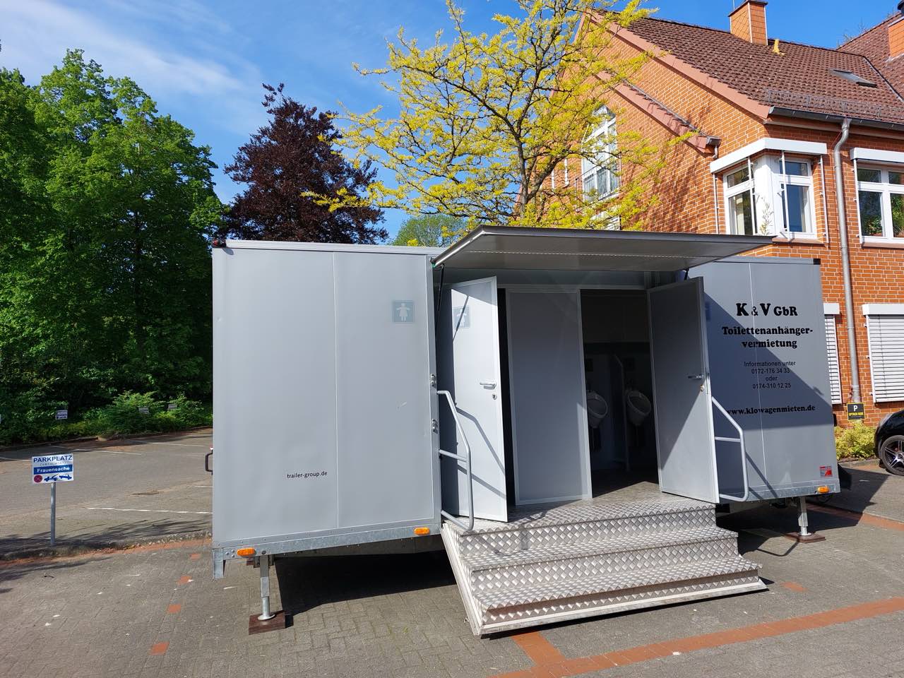 Geöffneter Toilettenanhänger auf einem Parkplatz vor einem Backsteingebäude