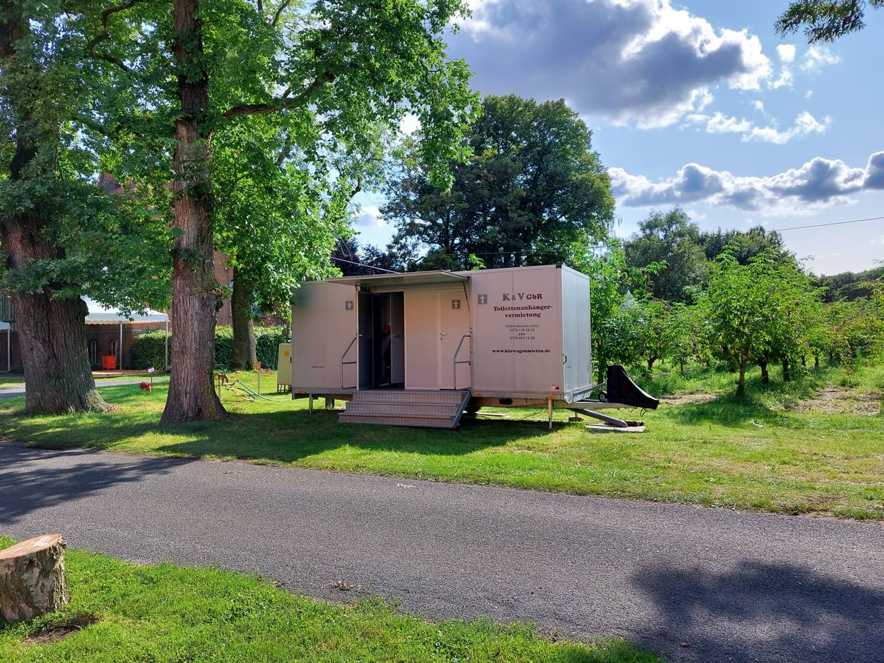 Toilettenanhänger auf einer Wiese zwischen alten Bäumen