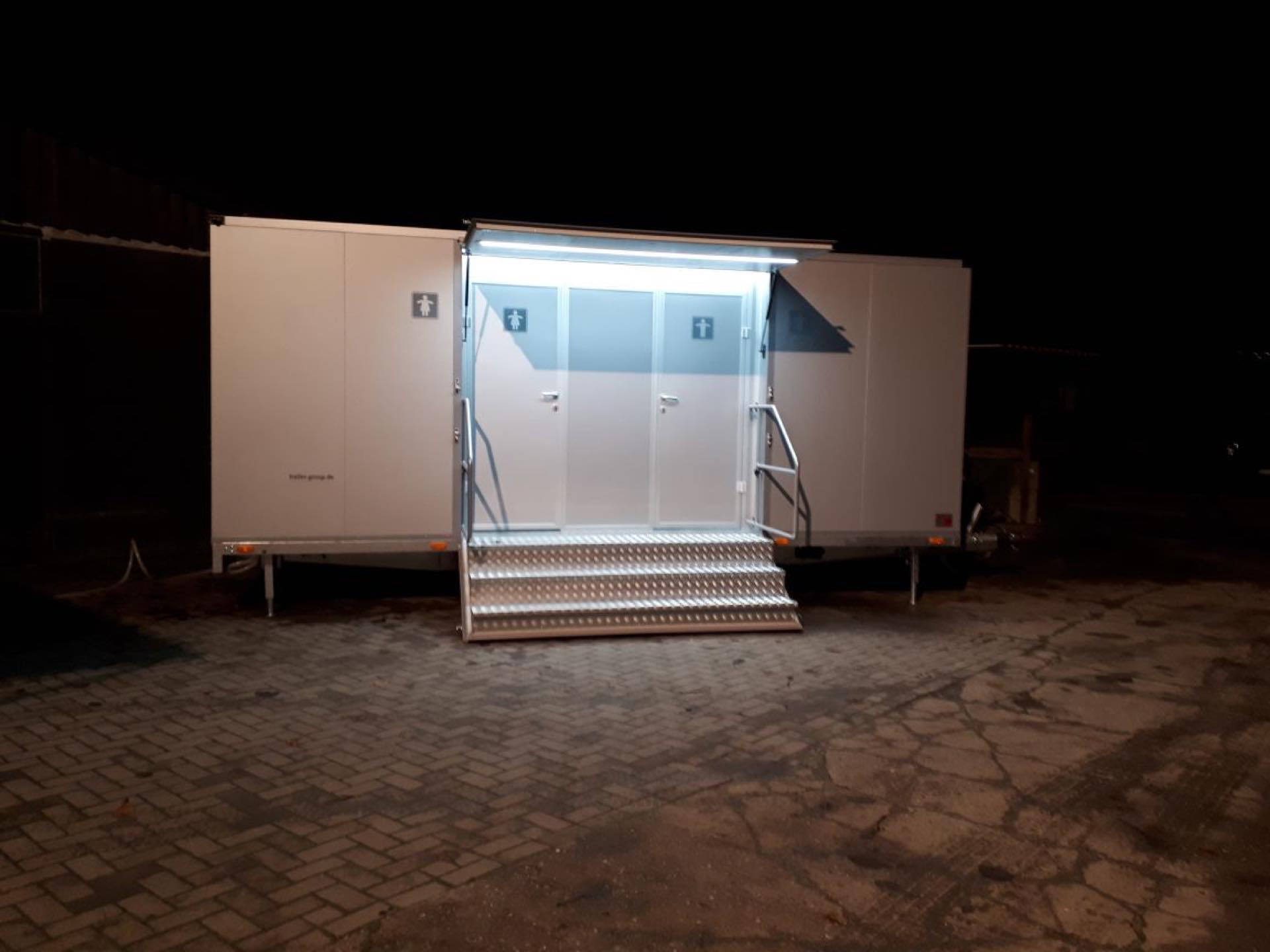 Nachts beleuchteter Toilettenanhänger mit warm ausgeleuchtetem Eingangsbereich