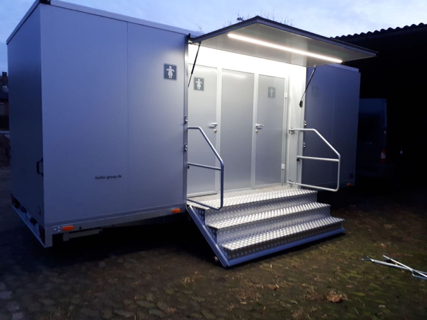 Toilettenanhänger in der Abenddämmerung mit beleuchtetem Eingangsbereich